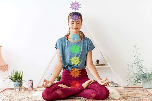 mindfulness, spirituality and healthy lifestyle concept - woman meditating in lotus pose at yoga studio with seven chakra symbols